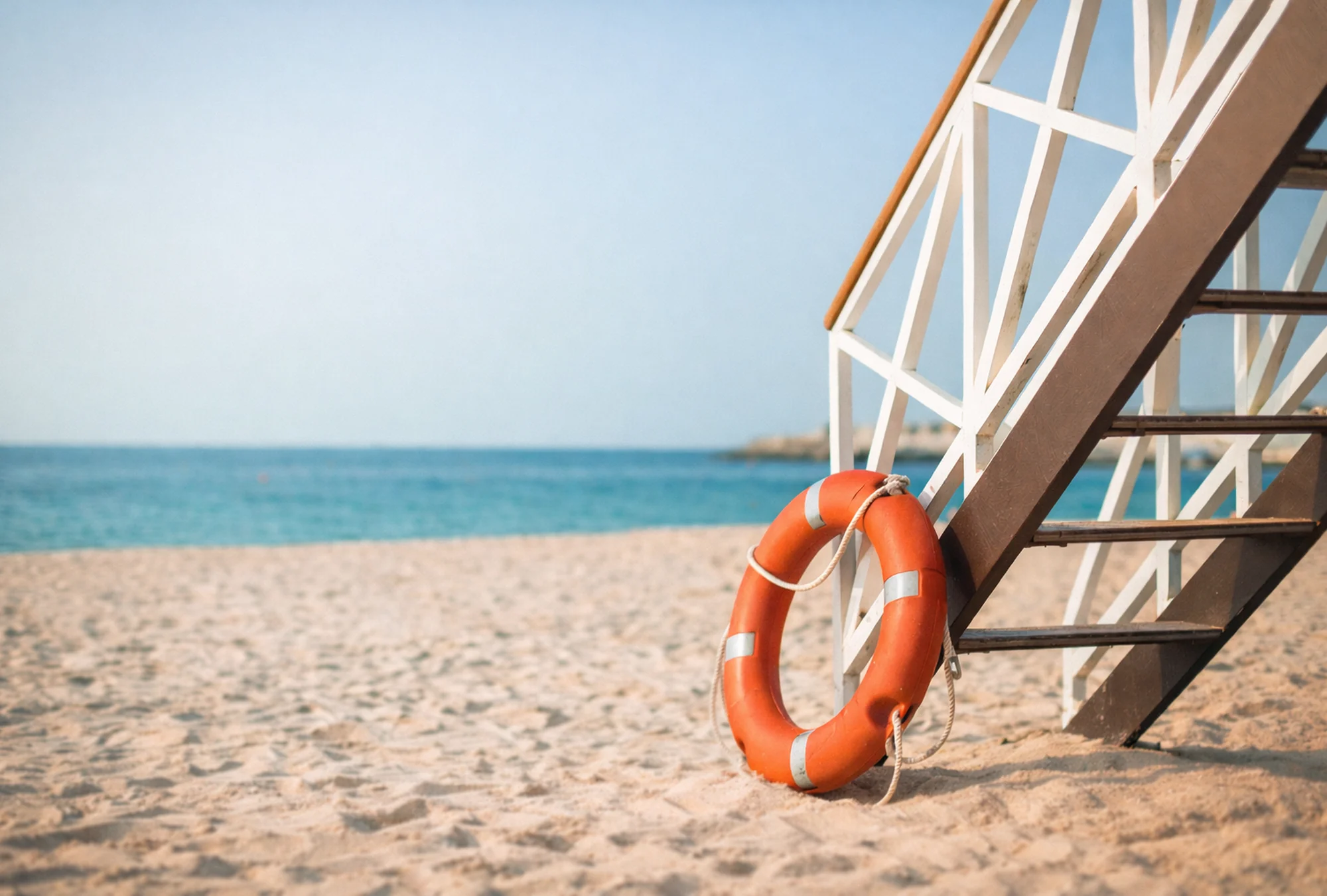 The ocean as viewed from beside a lifeguard tower with a life safety ring next to the stairs to the tower symbolizing the need for cautious monitoring and course correction.