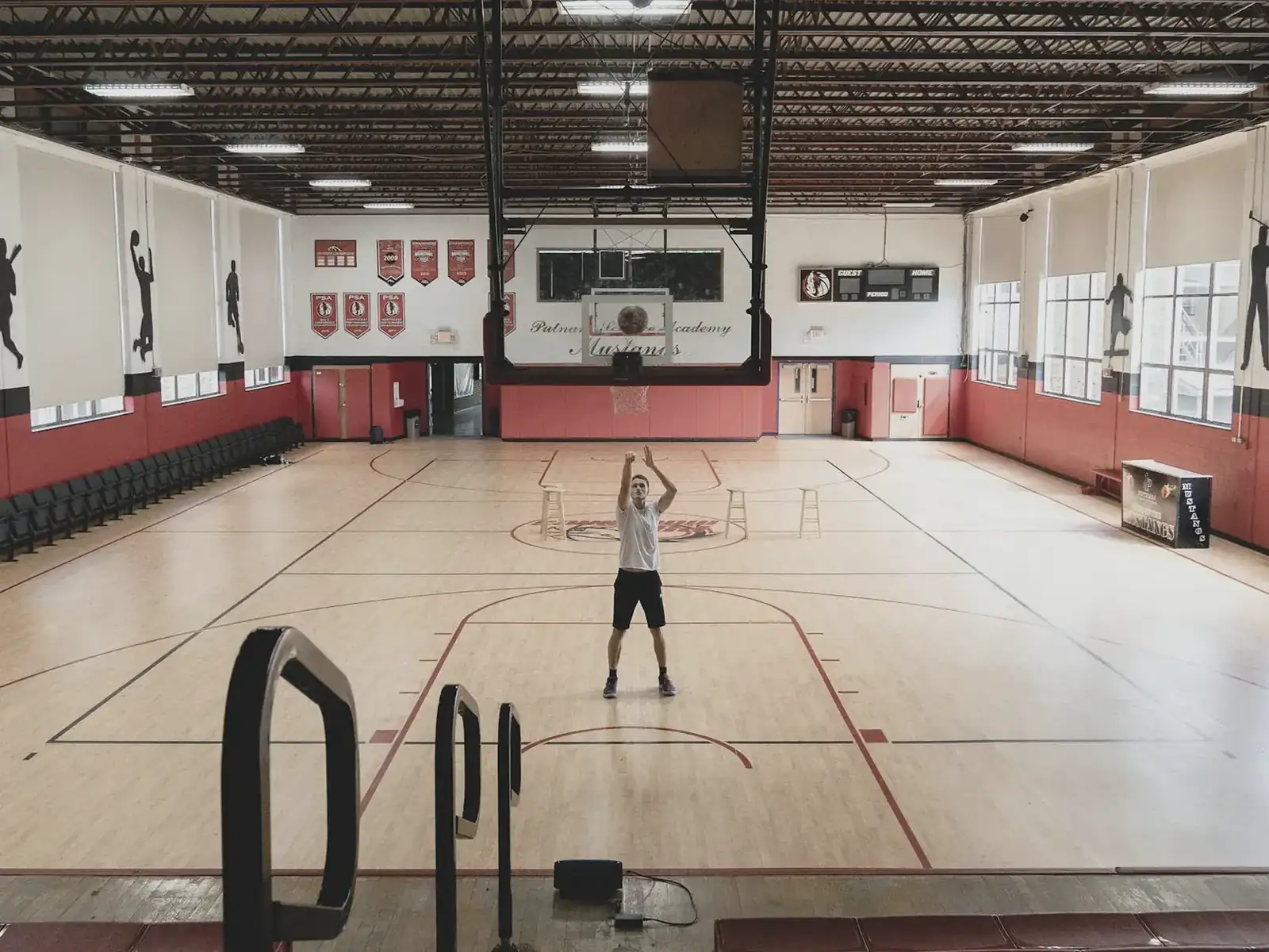 A lone athlete practicing basketball in an empty school gym long after others have left.