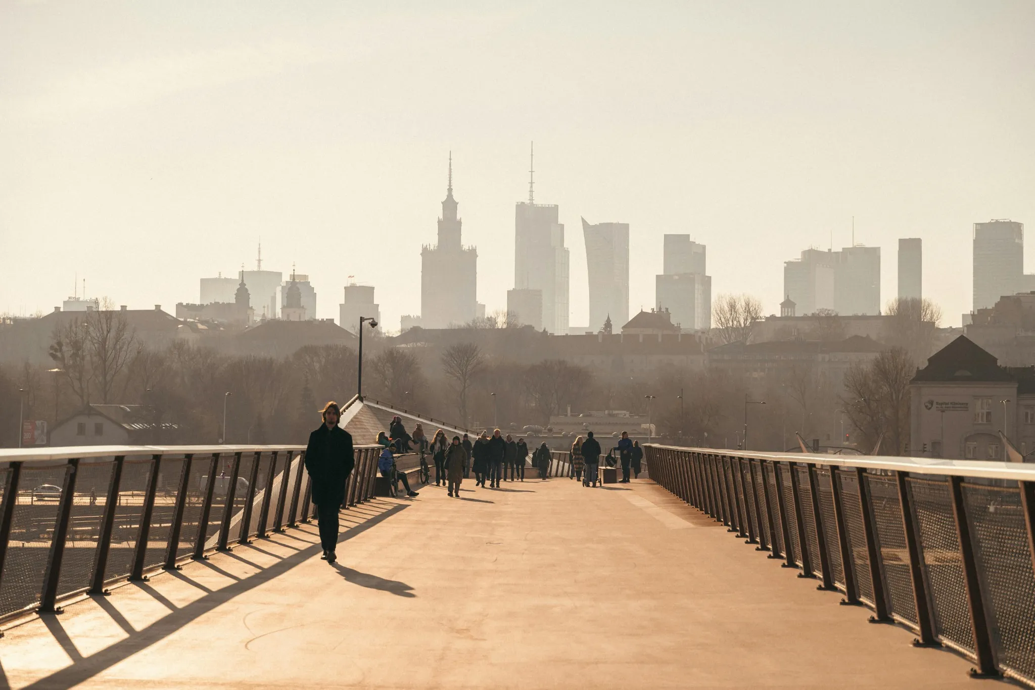 Frustrated pedestrian walking alone on a wide bridge after a long day with a hazy city skyline and tall buildings in the background